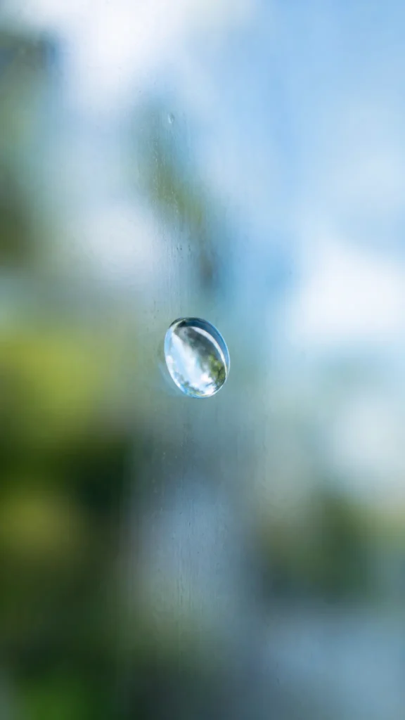 A water droplet on clean glass, reflecting soft natural light.
